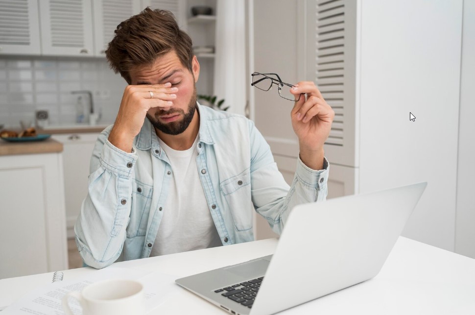 A person rubbing their eyes in front of a computer.